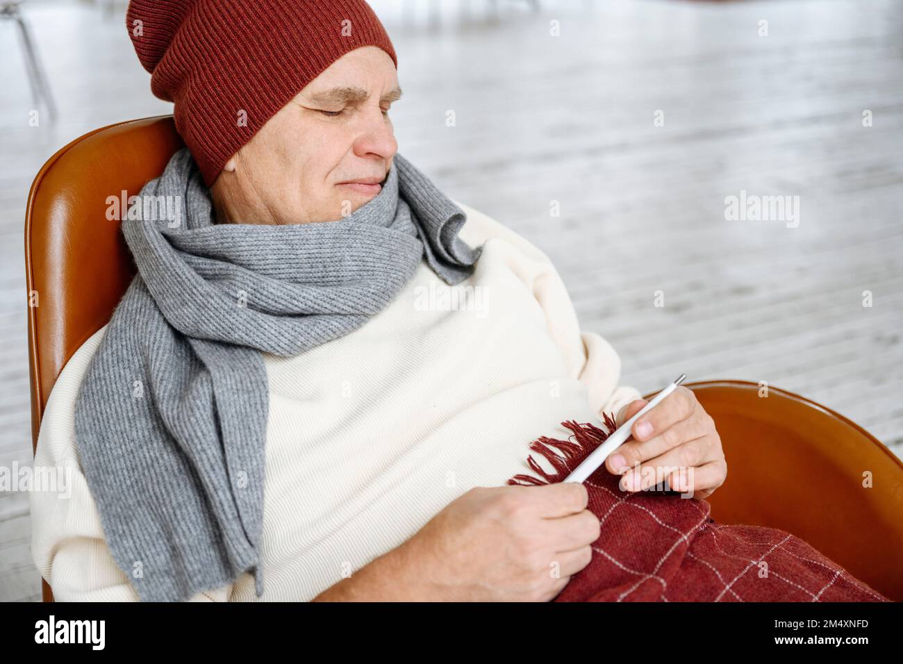 Ein älterer Mann trägt warme Kleidung und hält ein Thermometer Stockfoto