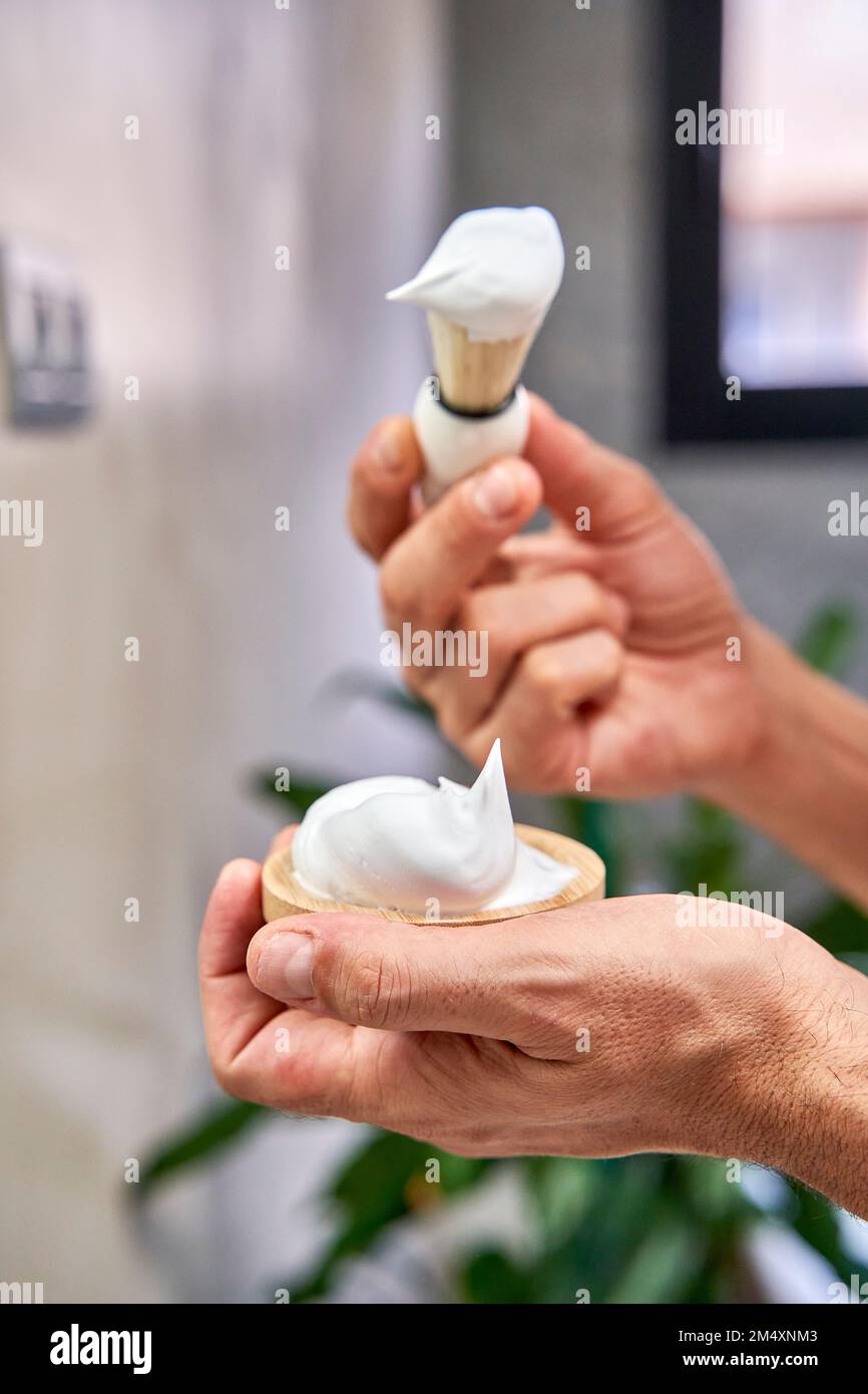 Hände eines Mannes mit Rasiercreme und Bürste im Badezimmer zu Hause Stockfoto
