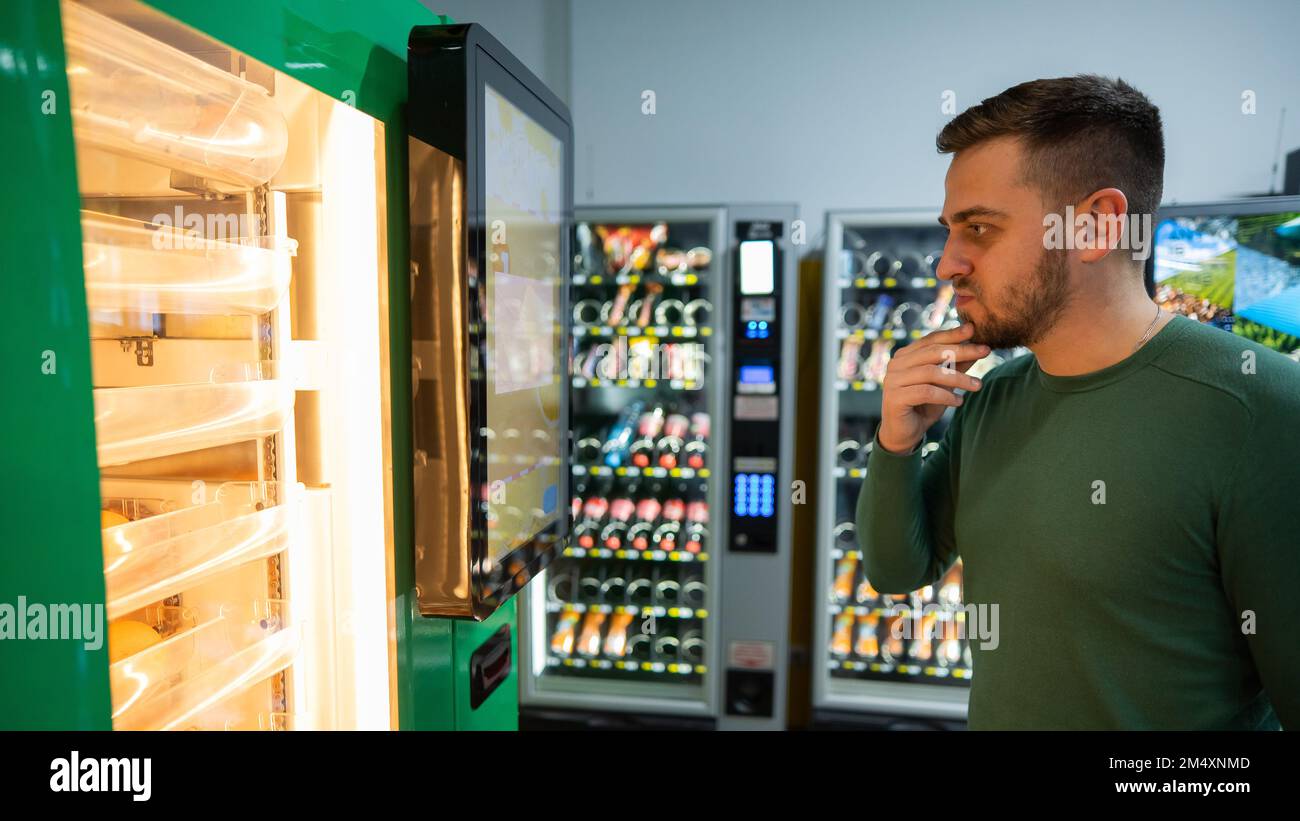 Ein weißer Mann kauft frisch gepressten Orangensaft aus dem Automaten. Stockfoto