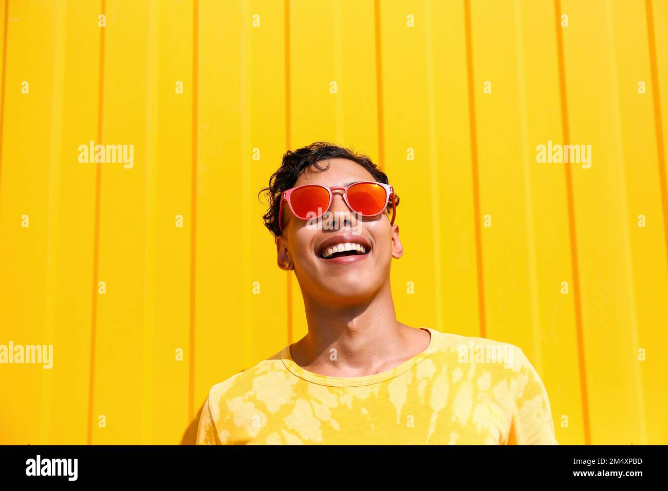 Ein glücklicher Mann, der vor der gelben Wand ein T-Shirt trägt Stockfoto