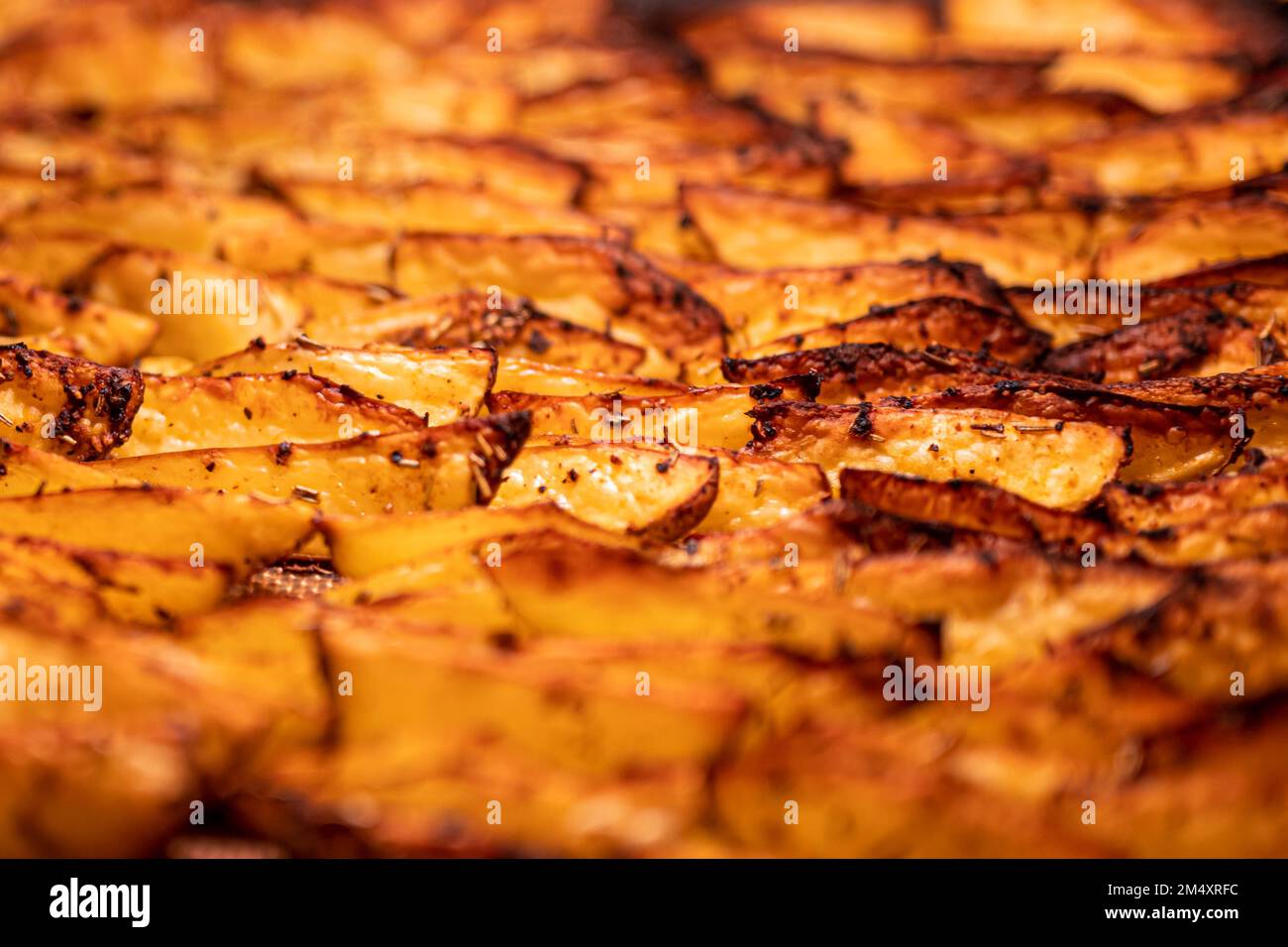 Beschreibung: Knusprige, goldbraune, gebackene Kartoffelkeile mit Paprika, Knoblauch, Salz, Pfeffer, Rosmarin, basilikum auf dem Tablett im Ofen, fotografiert von Stockfoto
