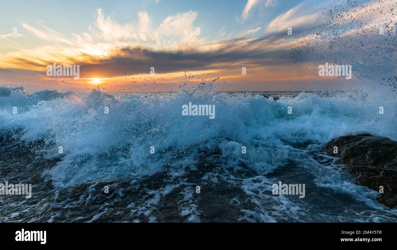 Eine von Sonnenaufgang beleuchtete Ocean Wave bricht an der Strandküste im hochauflösenden Bildformat auf Stockfoto