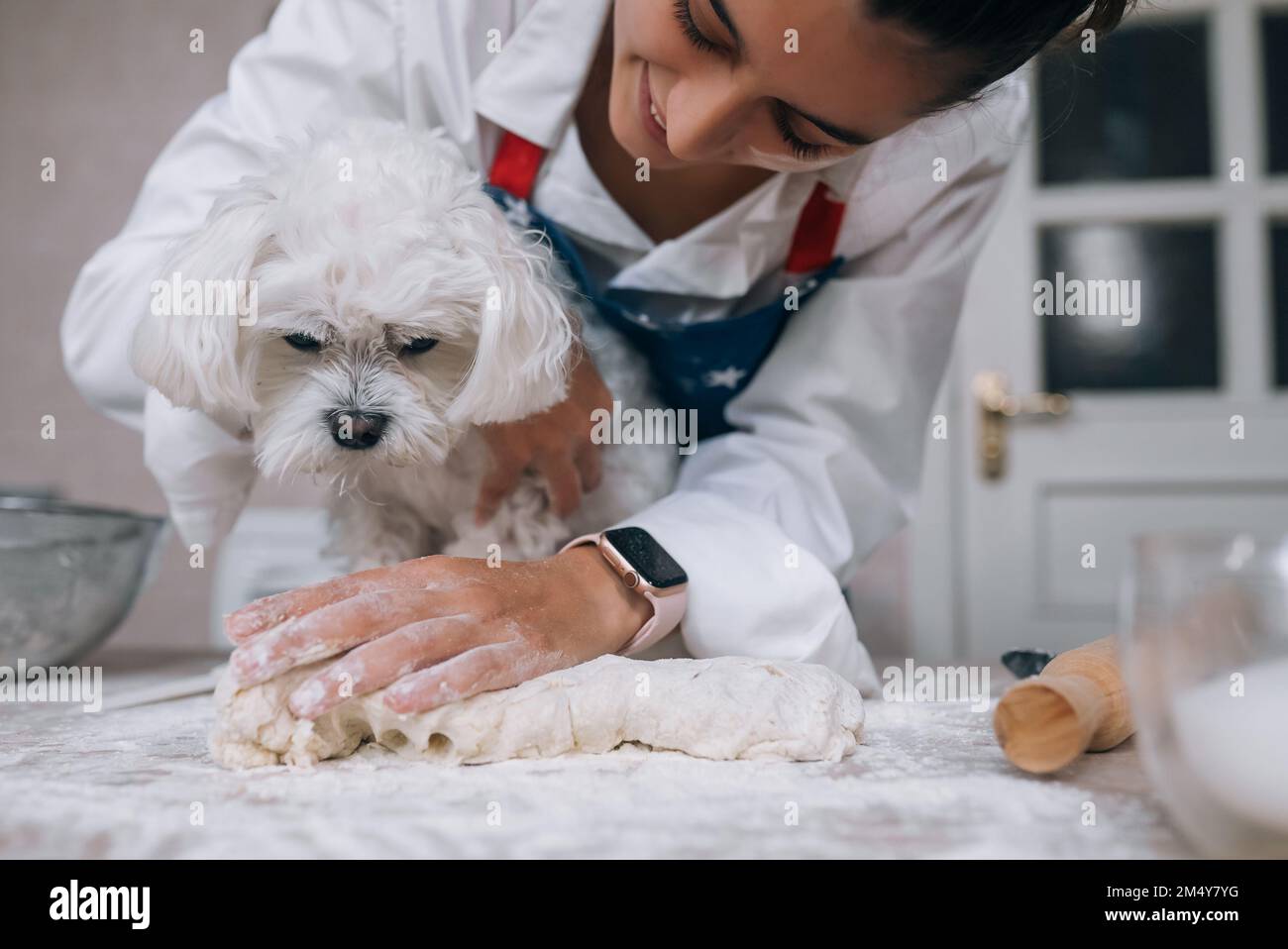 Frau in der Küche knetet den Teig mit ihrem Hund Stockfoto