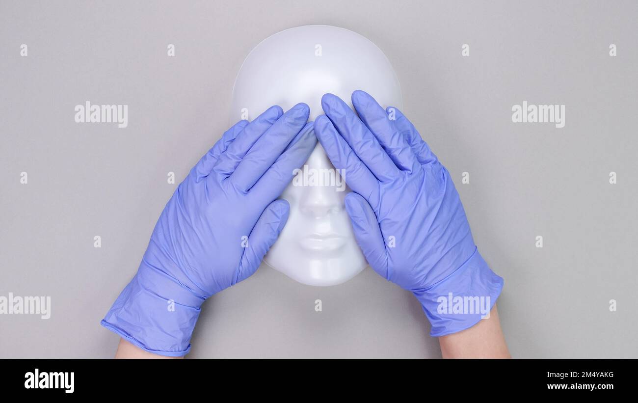 Hände in medizinischen Schutzhandschuhen bedeckte Augen des plastischen Schaufenstergesichts. Medizinische Handschuhe, Maske, Plastikgesicht Stockfoto
