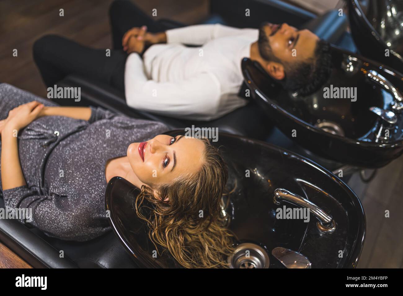 Zwei Personen, die Salon-Haare-Rückenwäsche benutzen. Eine weiße Frau und ein indischer Mann. Großer Blickwinkel. Speicherplatz kopieren. Friseurinnenraum. Hochwertiges Foto Stockfoto