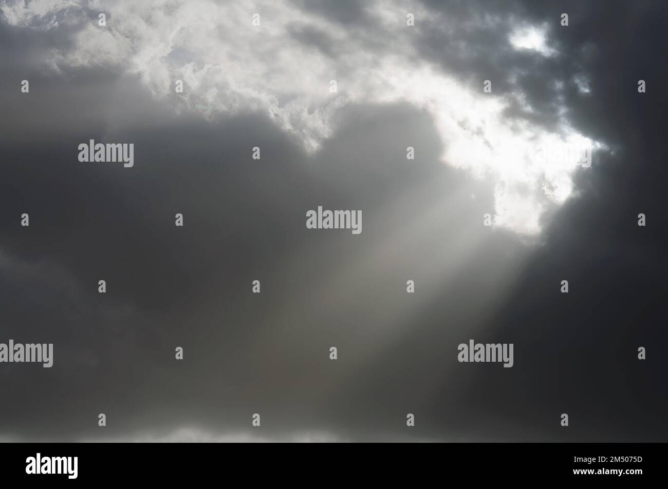 Düsterer, dunkler Himmel mit Lichtstrahlen, die durch die Wolken brechen. Dramatischer Himmel, Erleuchtung und Segen Stockfoto