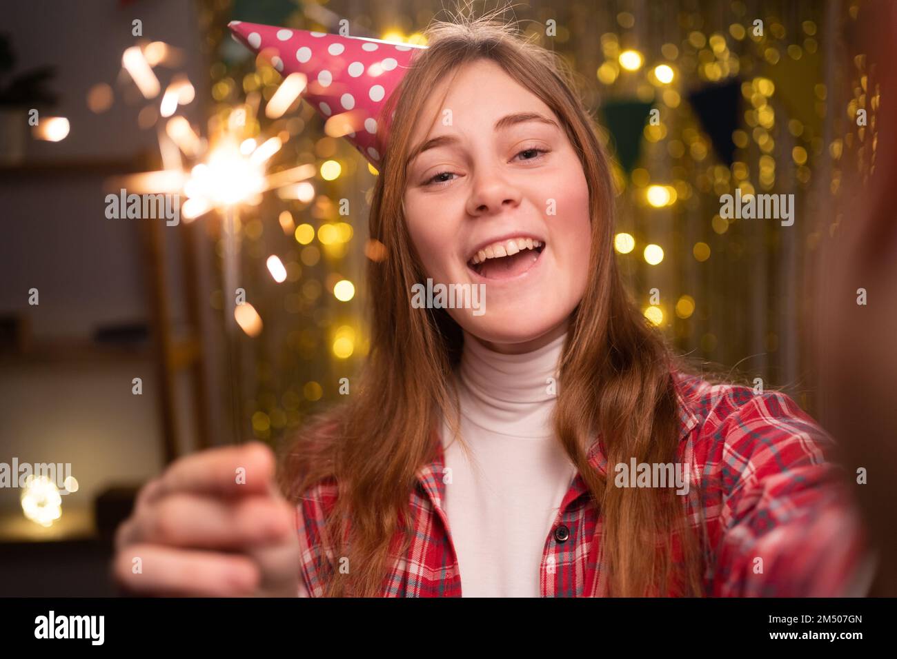 Mädchen mit glitzernden Lichtern an ihrem Geburtstag, während sie zu Hause feiert. Selfie in Party Cone hat und bengals Light, Geburtstagsparty-Konzept Stockfoto
