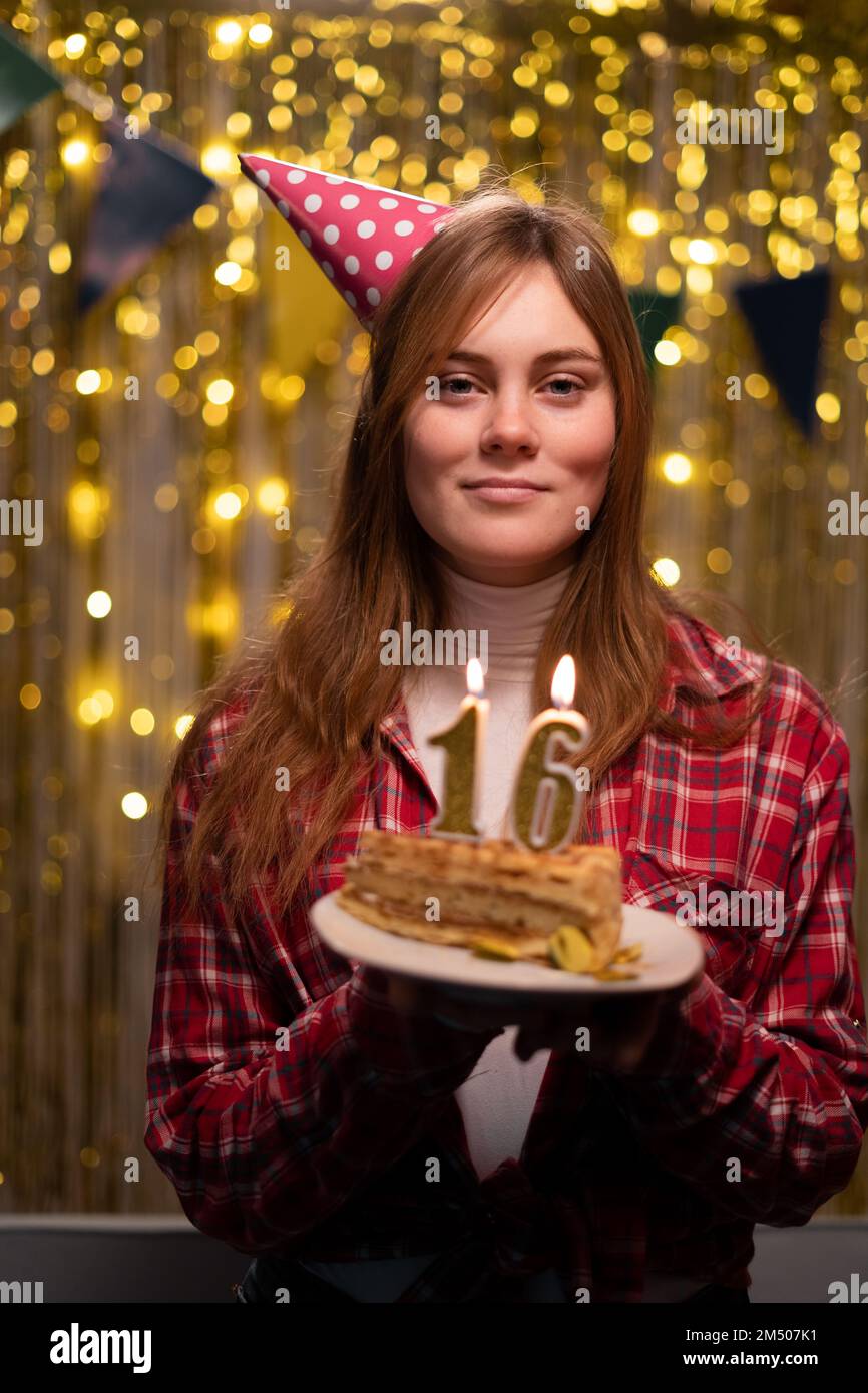 Geburtstagsfeier. Porträt einer fröhlichen jungen Frau, die Kerzen hochbläst 16 zum Geburtstag Kuchen trägt Cone Partyhut macht Wünsche Happy festlich Stimmung Cel Stockfoto