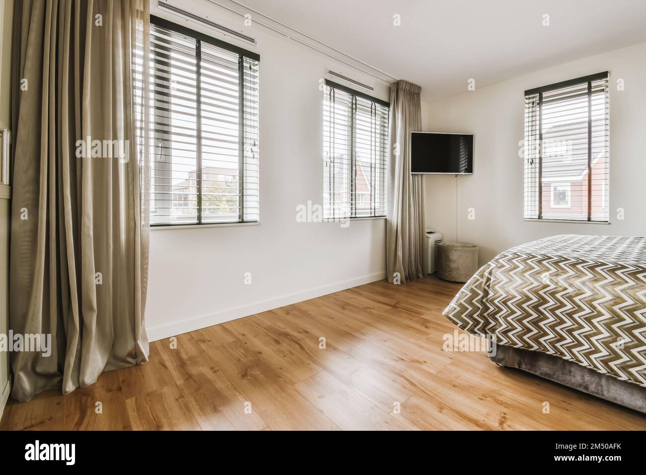 Ein Schlafzimmer mit Holzfußboden und großen Fenstern, die auf die Stadtlandschaft blicken Stockfoto