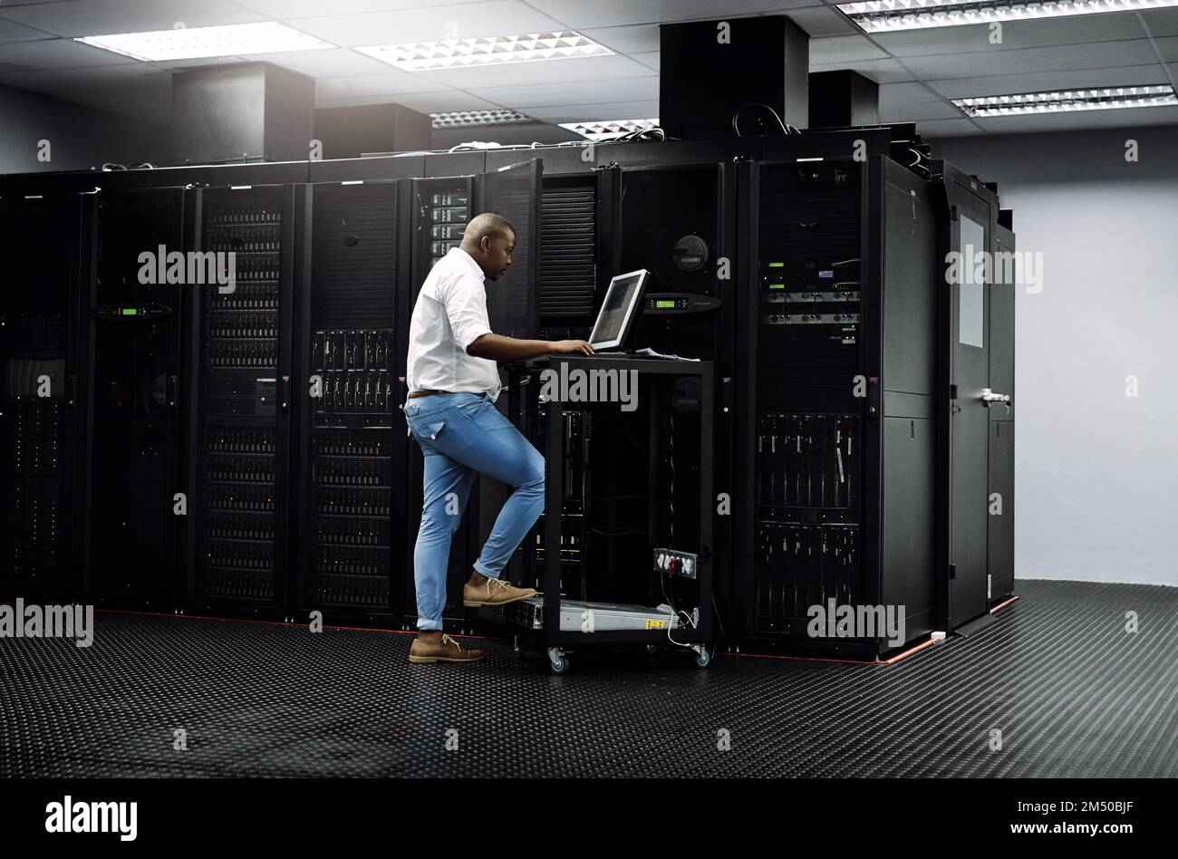 Aktualisieren der Software. Gesamtbild eines IT-Technikers, der einen Computer verwendet, während er im Serverraum eines Rechenzentrums arbeitet. Stockfoto