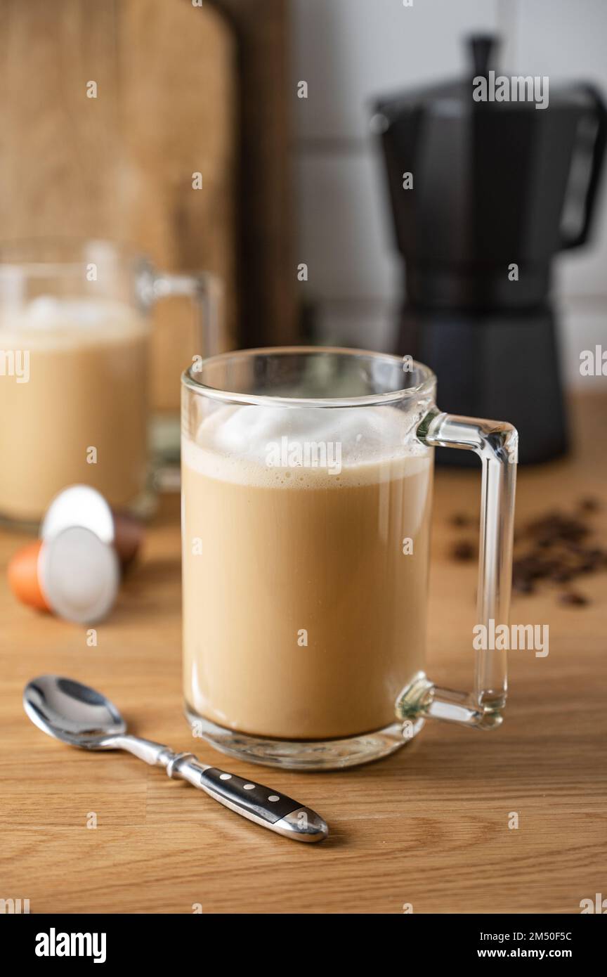 Zwei Tassen frisch gebrühten aromatischen Kaffees mit Milch auf dem Küchentisch mit einer Kaffeekanne und verstreuten Körnern. Das Konzept einer Frühmorgenbrasse Stockfoto