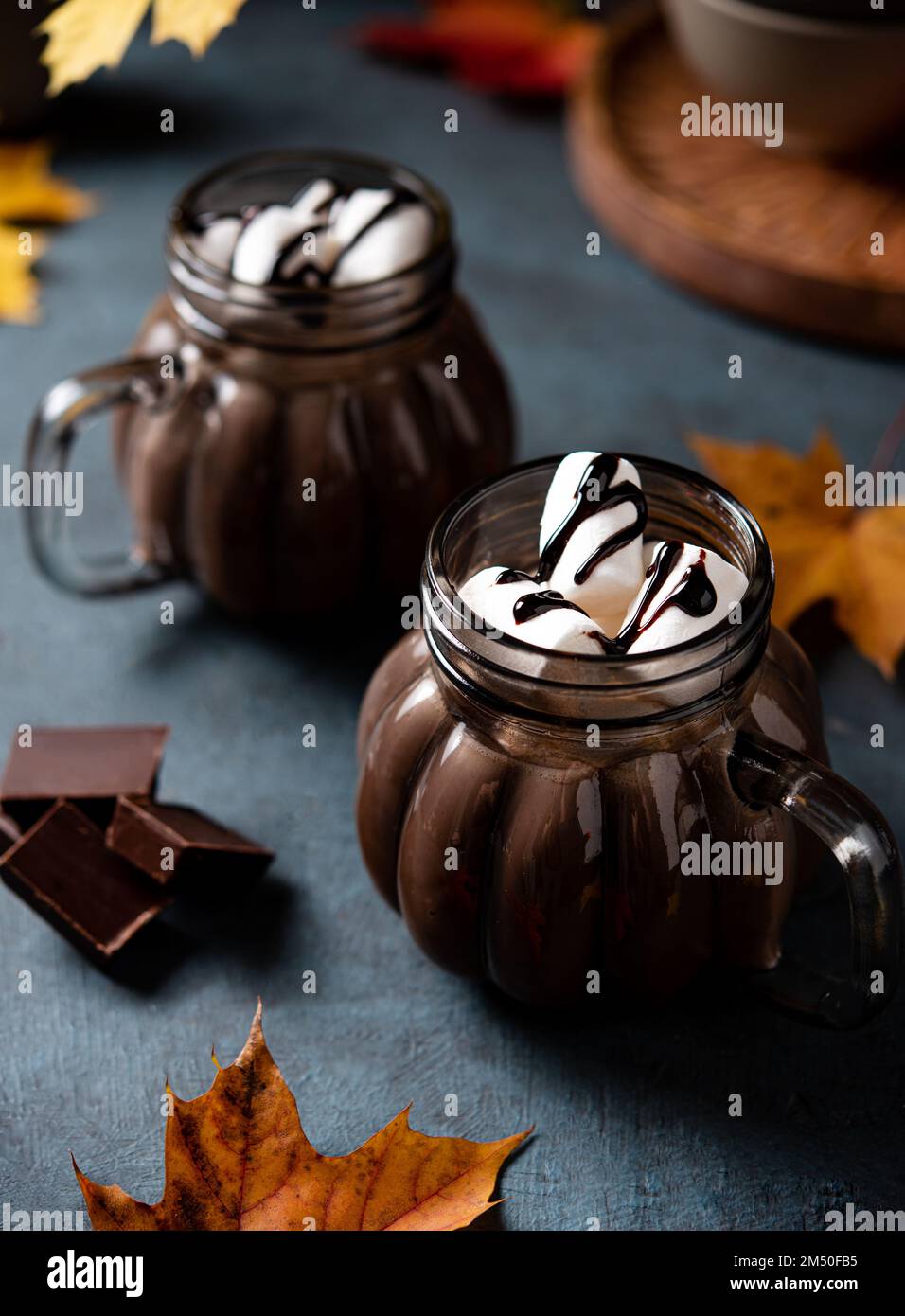 Zwei Tassen aromatische heiße Schokolade mit Marshmallows auf dunklem Hintergrund mit Ahornblättern im Herbst. Konzept gemütlicher Drink. Stockfoto