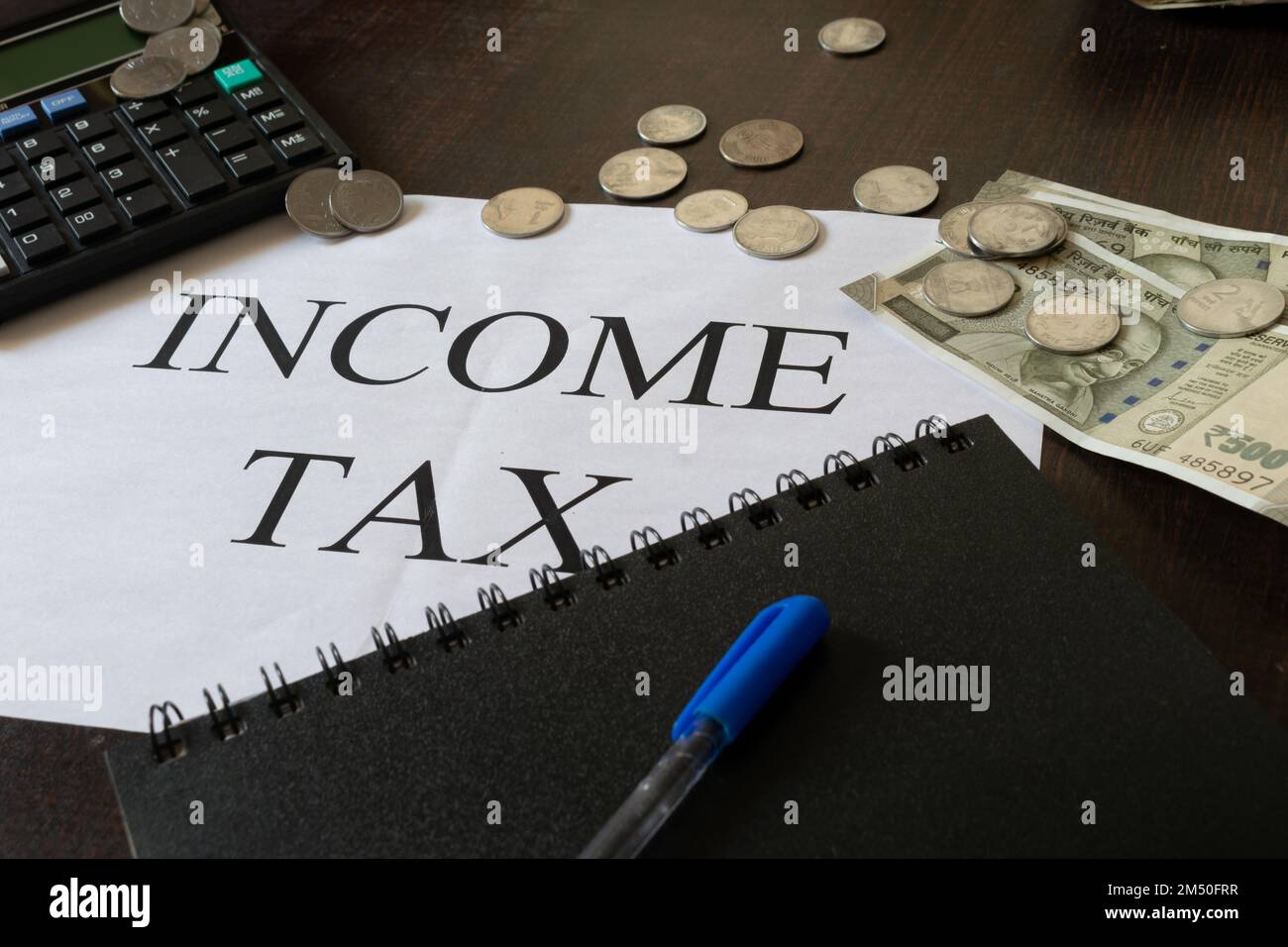 Bild der Einkommensteuer auf einer Seite mit Taschenrechner, Tagebuch, Bargeld, Stift und einer Tasse Infosys. Budget, Einkommensteuererklärung, Einreichung, Geschäft, Job, savi Stockfoto