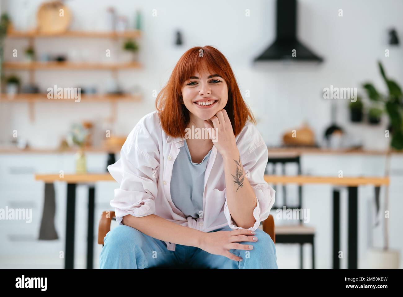 Porträt einer wunderschönen Frau, die auf einem Stuhl in einer modernen Küche im Hintergrund sitzt Stockfoto