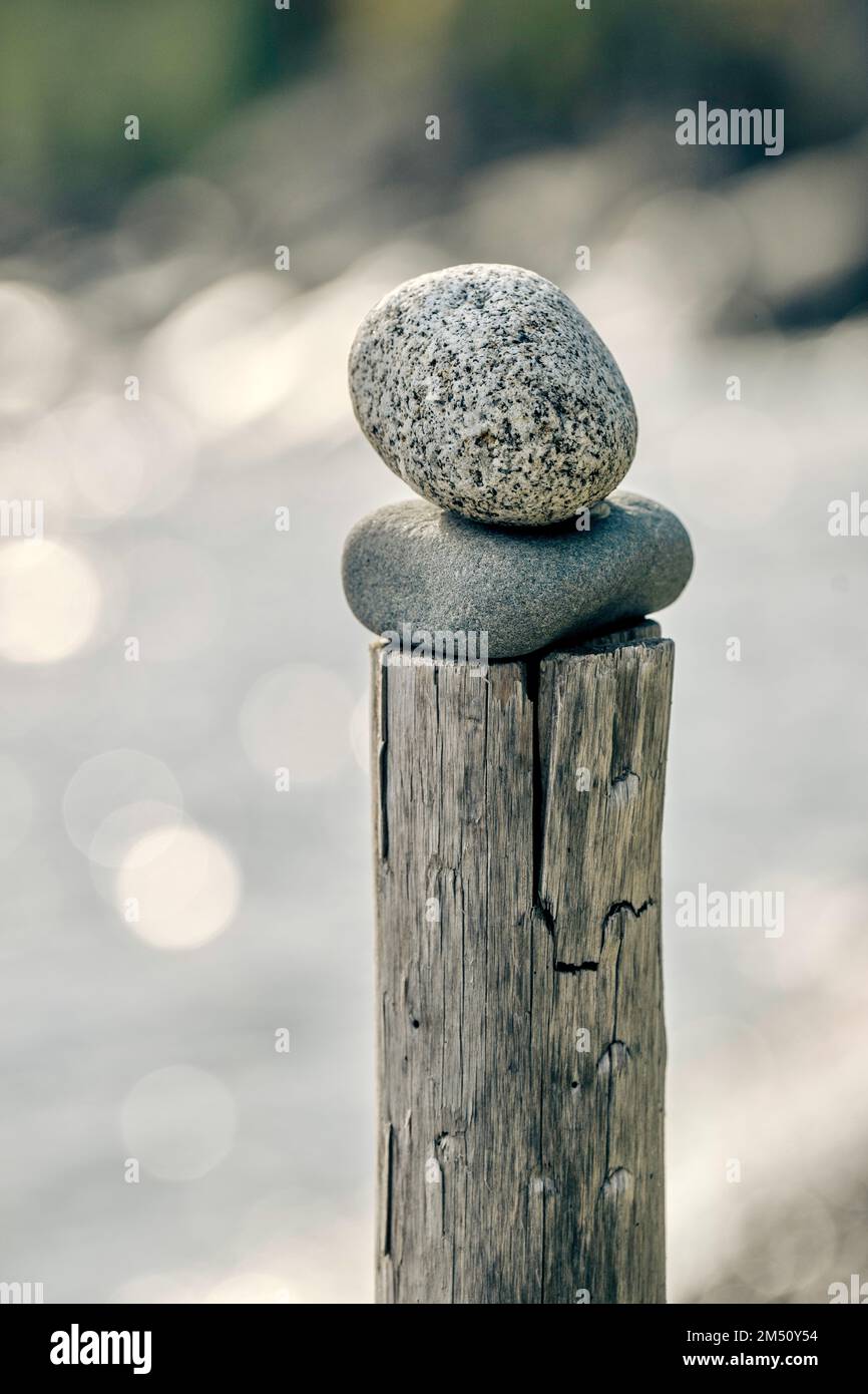 Eine vertikale Nahaufnahme von zwei Steinen, die auf einem alten Holzpfahl auf einem isolierten Hintergrund gestapelt sind Stockfoto
