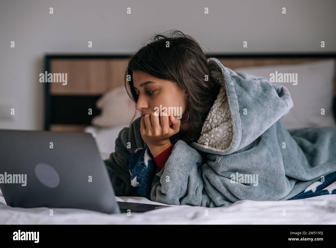Junge Frau, die am Laptop arbeitet, während sie auf dem Bett liegt Stockfoto