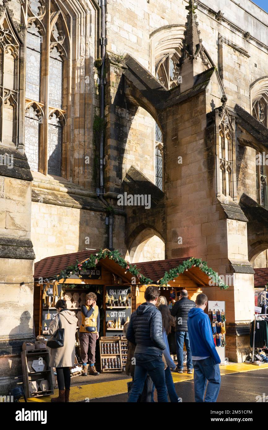 Weihnachtseinkäufer auf dem Winchester Christmas Market mit Ständen zwischen fliegenden Steinen der gotischen Winchester Cathedral, England, Großbritannien Stockfoto