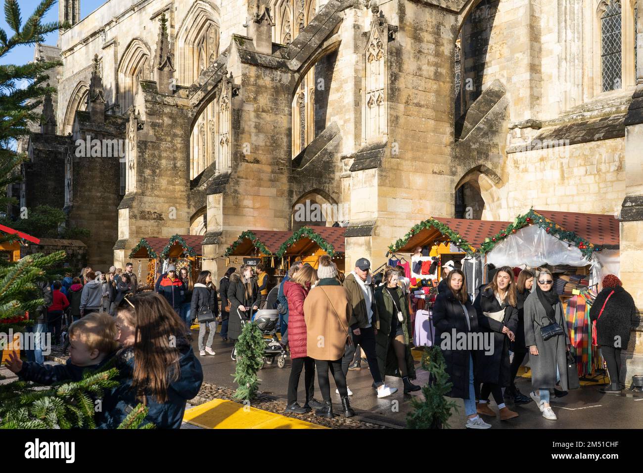 Weihnachtseinkäufer auf dem Winchester Christmas Market mit Ständen zwischen fliegenden Steinen der gotischen Winchester Cathedral, England, Großbritannien Stockfoto