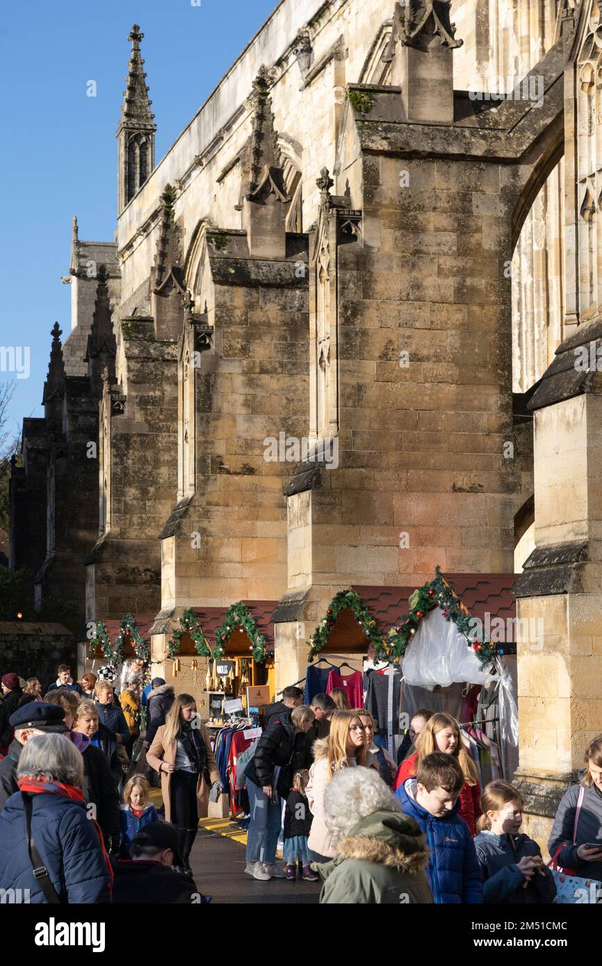 Weihnachtseinkäufer auf dem Winchester Christmas Market mit Ständen zwischen fliegenden Steinen der gotischen Winchester Cathedral, England, Großbritannien Stockfoto