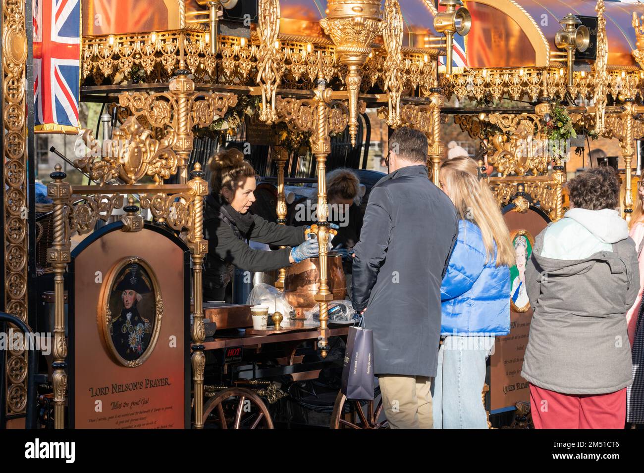 Traditioneller goldvergoldeter Glühwein und Churro-Stand, an dem Menschen außerhalb der Winchester Cathedral zu Weihnachten warme Getränke und Speisen serviert werden. England, Großbritannien Stockfoto