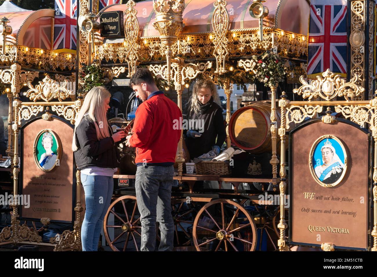 Traditioneller goldvergoldeter Glühwein und Churro-Stand, an dem Menschen außerhalb der Winchester Cathedral zu Weihnachten warme Getränke und Speisen serviert werden. England, Großbritannien Stockfoto