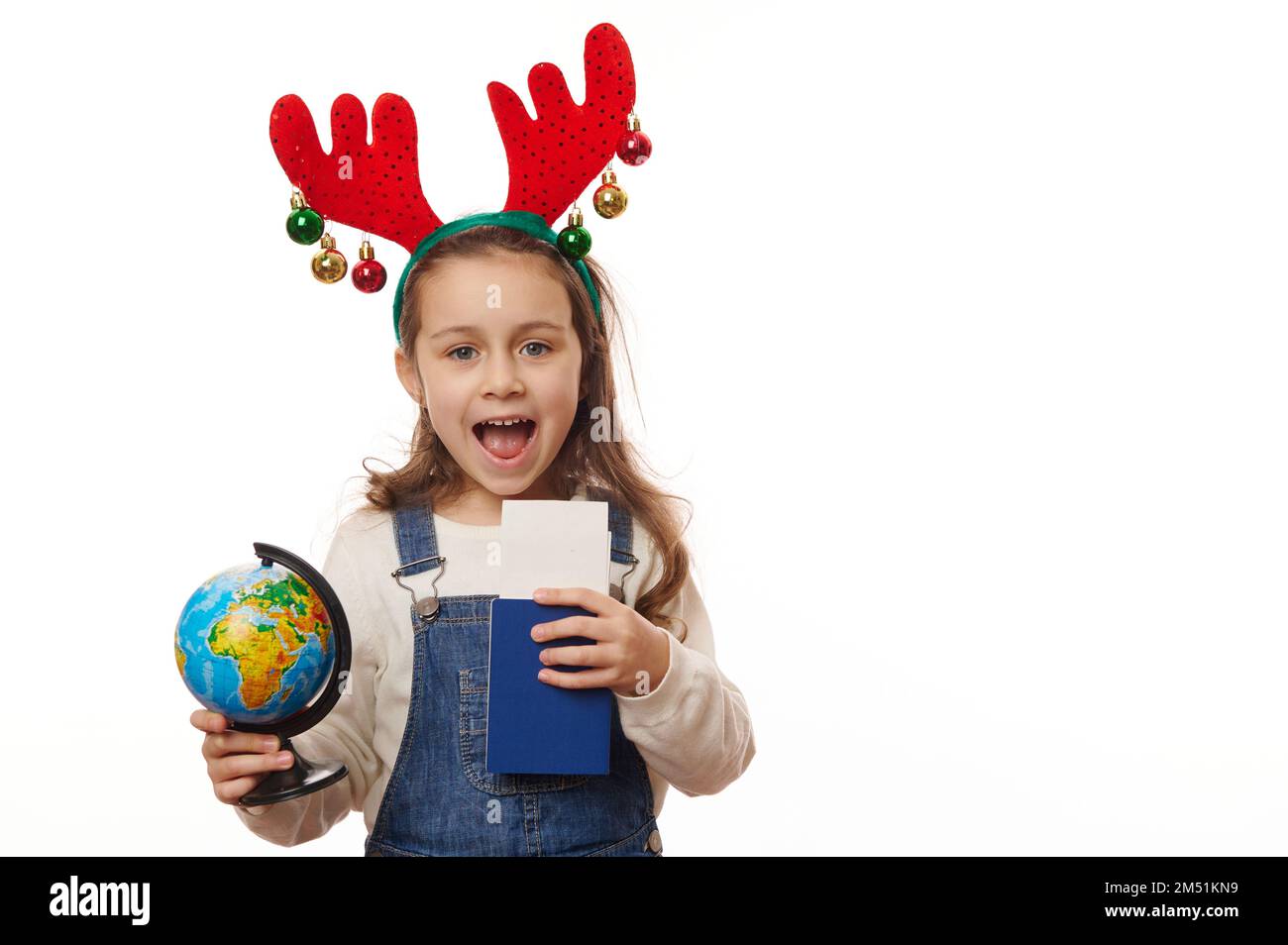 Ein bezauberndes kleines Mädchen mit Hirschgeweih, einem Globus und einer Bordkarte auf weißem Hintergrund. Reisekonzept Stockfoto