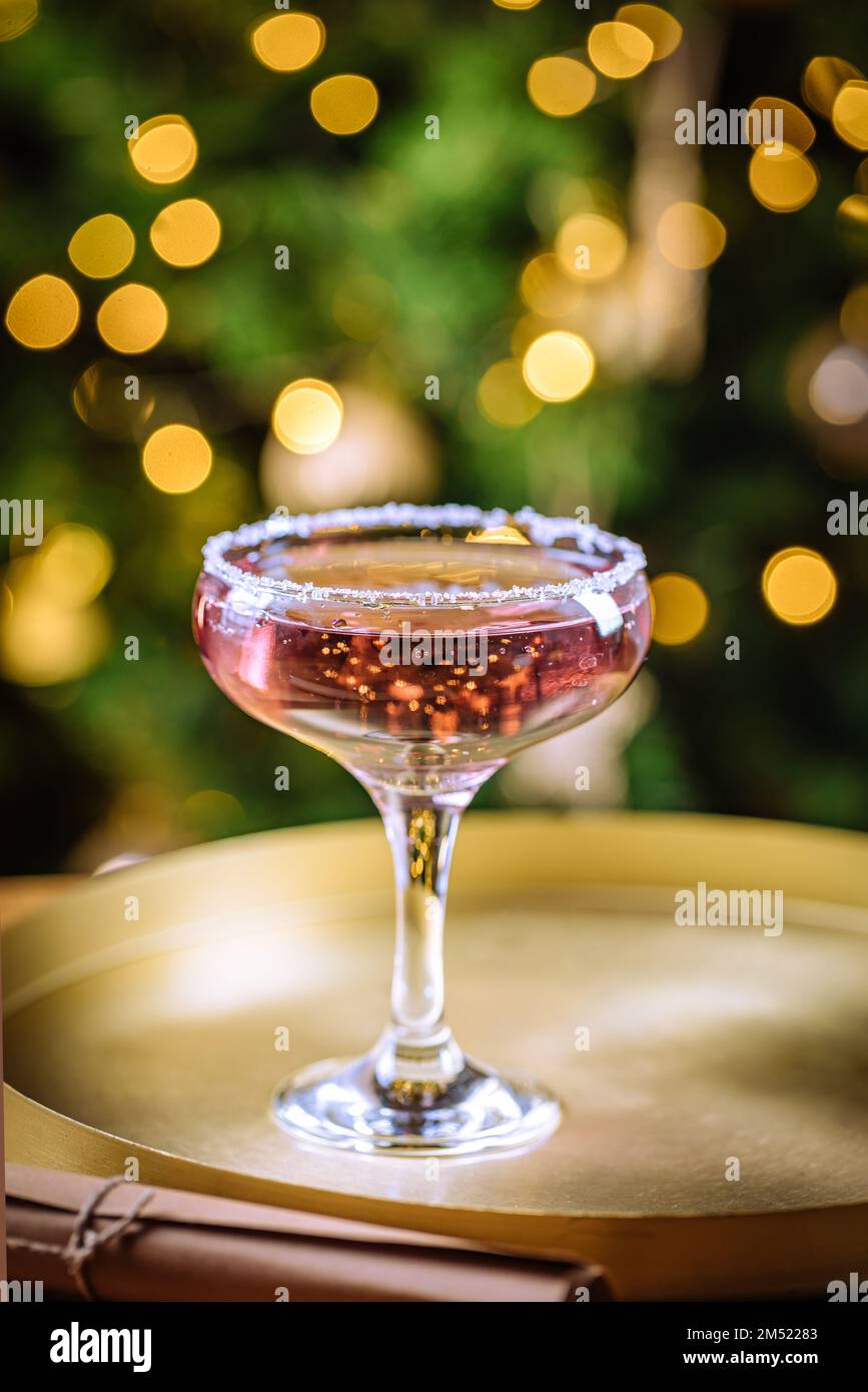 Rosencocktail in Coupé-Glas mit Mineralwasser. Weihnachtsbeleuchtung im Hintergrund. Stockfoto