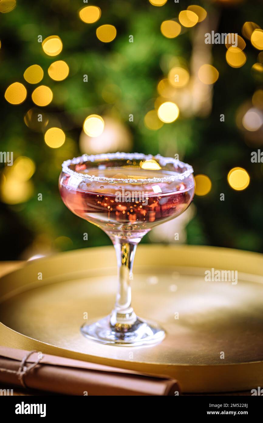 Rosencocktail in Coupé-Glas mit Mineralwasser. Weihnachtsbeleuchtung im Hintergrund. Stockfoto
