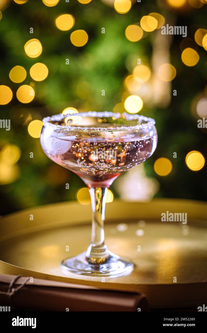 Rosencocktail in Coupé-Glas mit Mineralwasser. Weihnachtsbeleuchtung im Hintergrund. Stockfoto