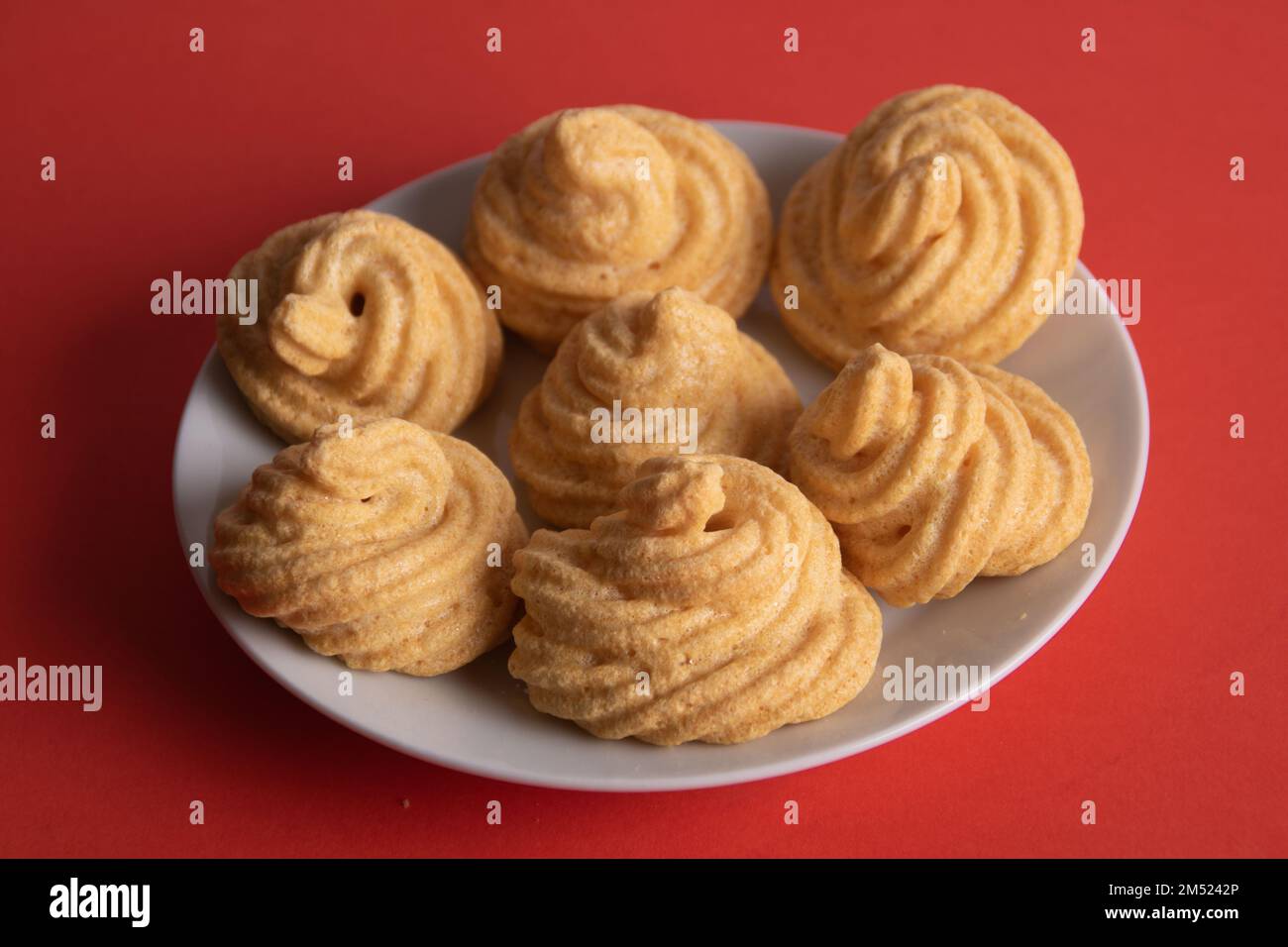 Foto eines Baiser, das aussieht wie eine Spirale, die auf einem Teller auf rotem Hintergrund liegt Stockfoto