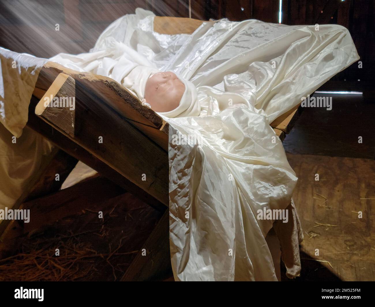 Jesus-Baby-Puppe schläft in einer rustikalen Scheunenmanger mit Lichtstrahlen Stockfoto