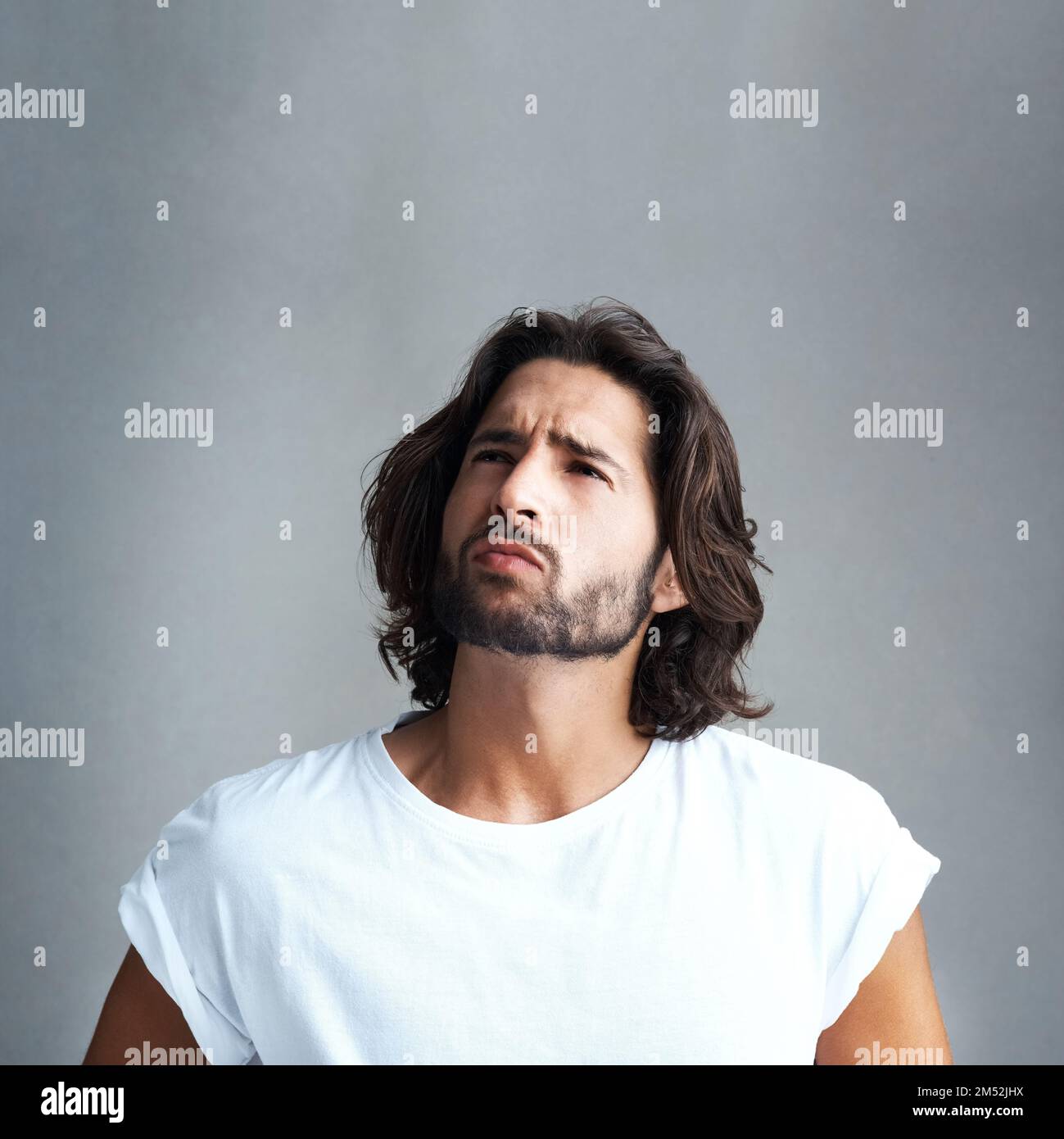 Was bedeutet das alles? Studioaufnahme eines gutaussehenden jungen Mannes, der vor grauem Hintergrund besorgt aussieht. Stockfoto