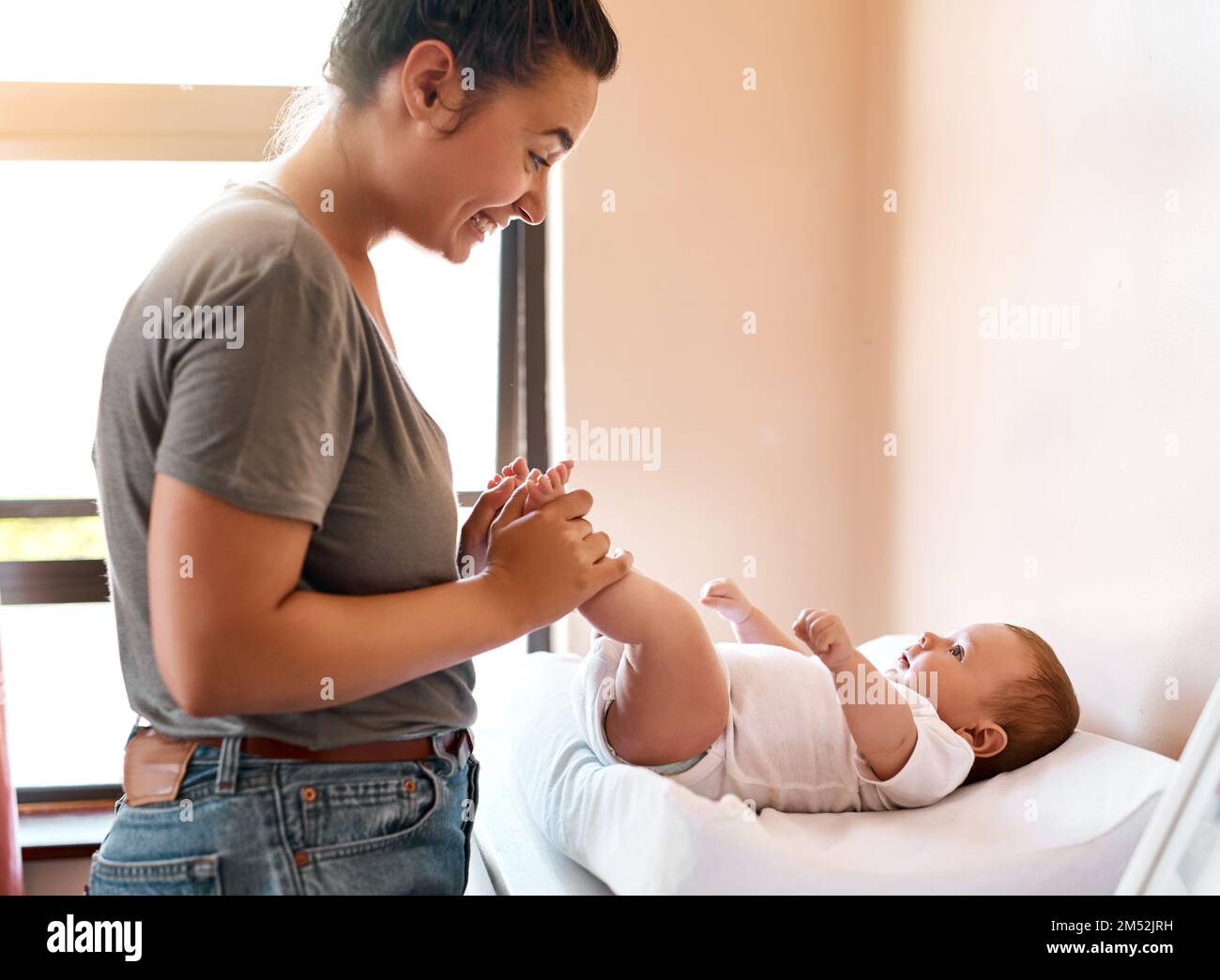 Braucht das Baby einen Windelwechsel? Eine junge Frau, die sich mit ihrem kleinen Jungen zu Hause anfreundet. Stockfoto