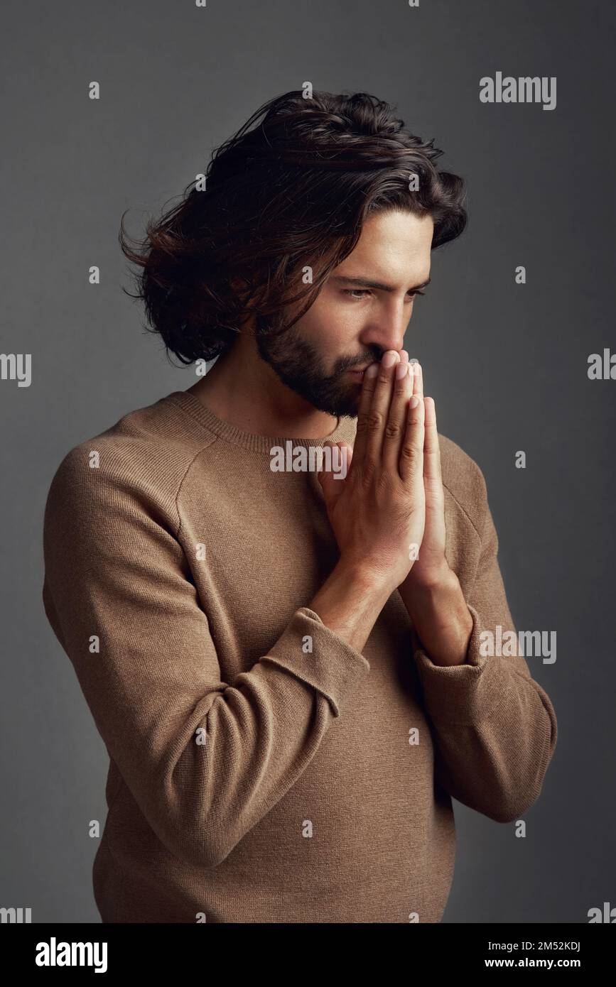 Ich habe mich verirrt und weiß nicht, was ich tun soll. Studioaufnahme eines gutaussehenden jungen Mannes, der vor grauem Hintergrund betet. Stockfoto