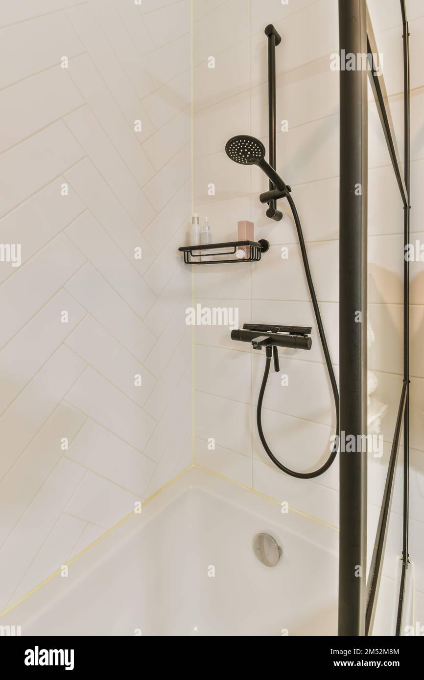 Ein Badezimmer mit weißen Fliesen und schwarzen Duschhähnen an der Wand neben der Badewanne ist ein Handgriff Stockfoto