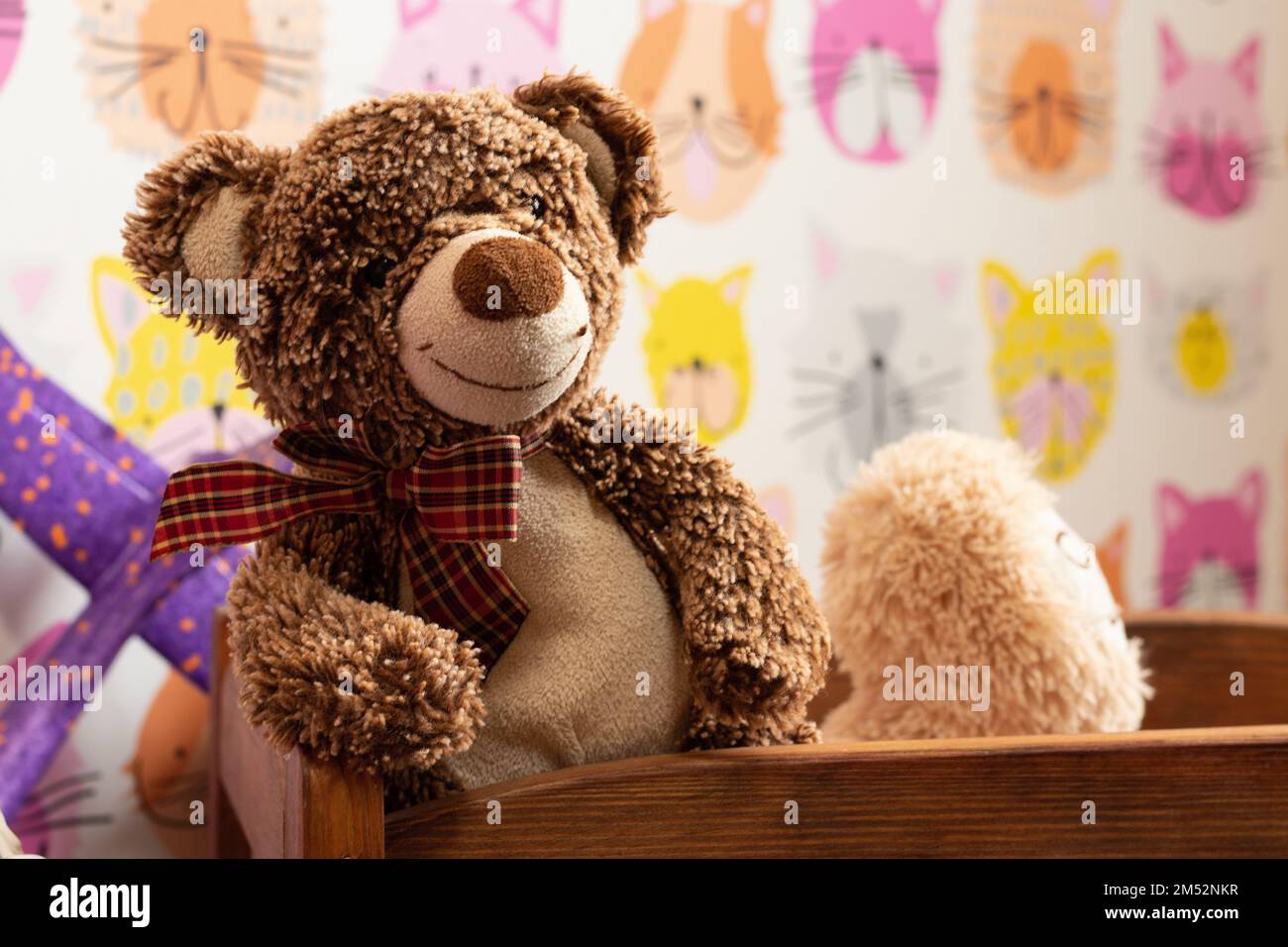 Ein weicher brauner Teddybär sitzt in einem Holzbett für Kinder im Kinderzimmer auf einem verschwommenen Hintergrund Stockfoto