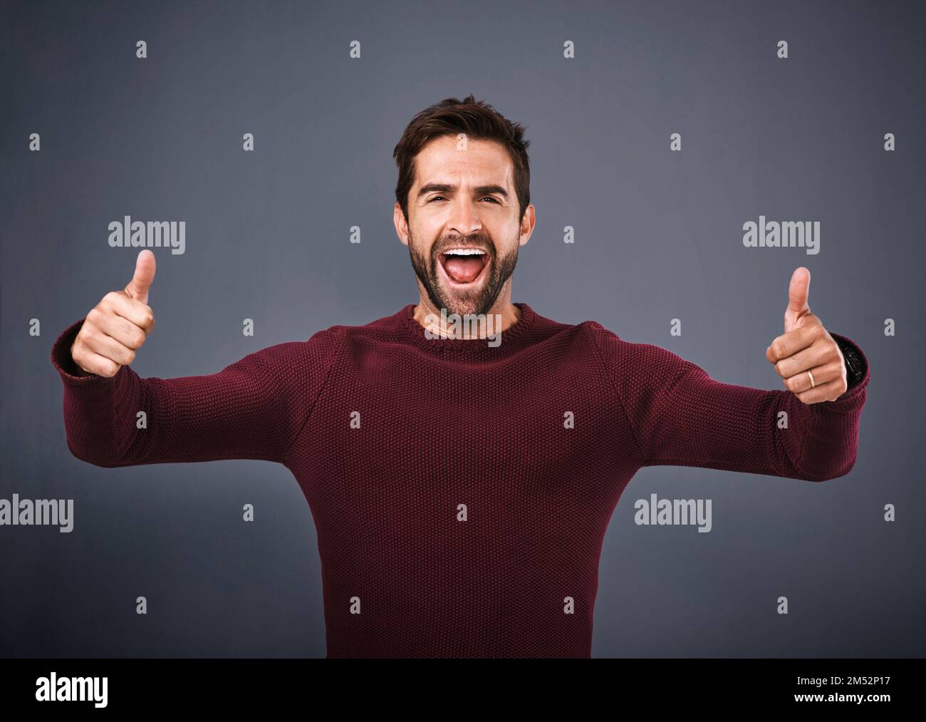 Super enthusiastisch. Studioaufnahme eines begeisterten jungen Mannes, der vor grauem Hintergrund zwei Daumen nach oben zeigt. Stockfoto