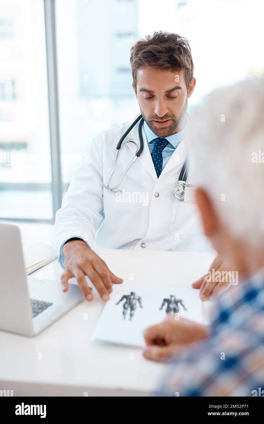 Lass mich dir das erklären. Ein gutaussehender junger Arzt, der einen Patienten in seiner Praxis berät. Stockfoto