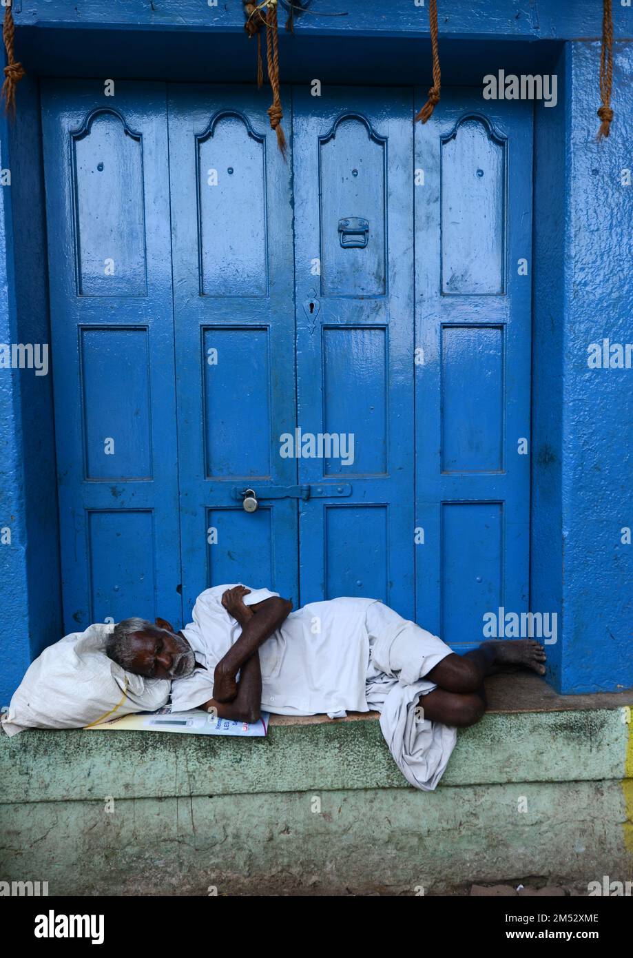 Ein tamilischer Mann macht ein Nickerchen an einer blauen Tür im Zentrum von Madurai, Tamil Nadu, Indien. Stockfoto