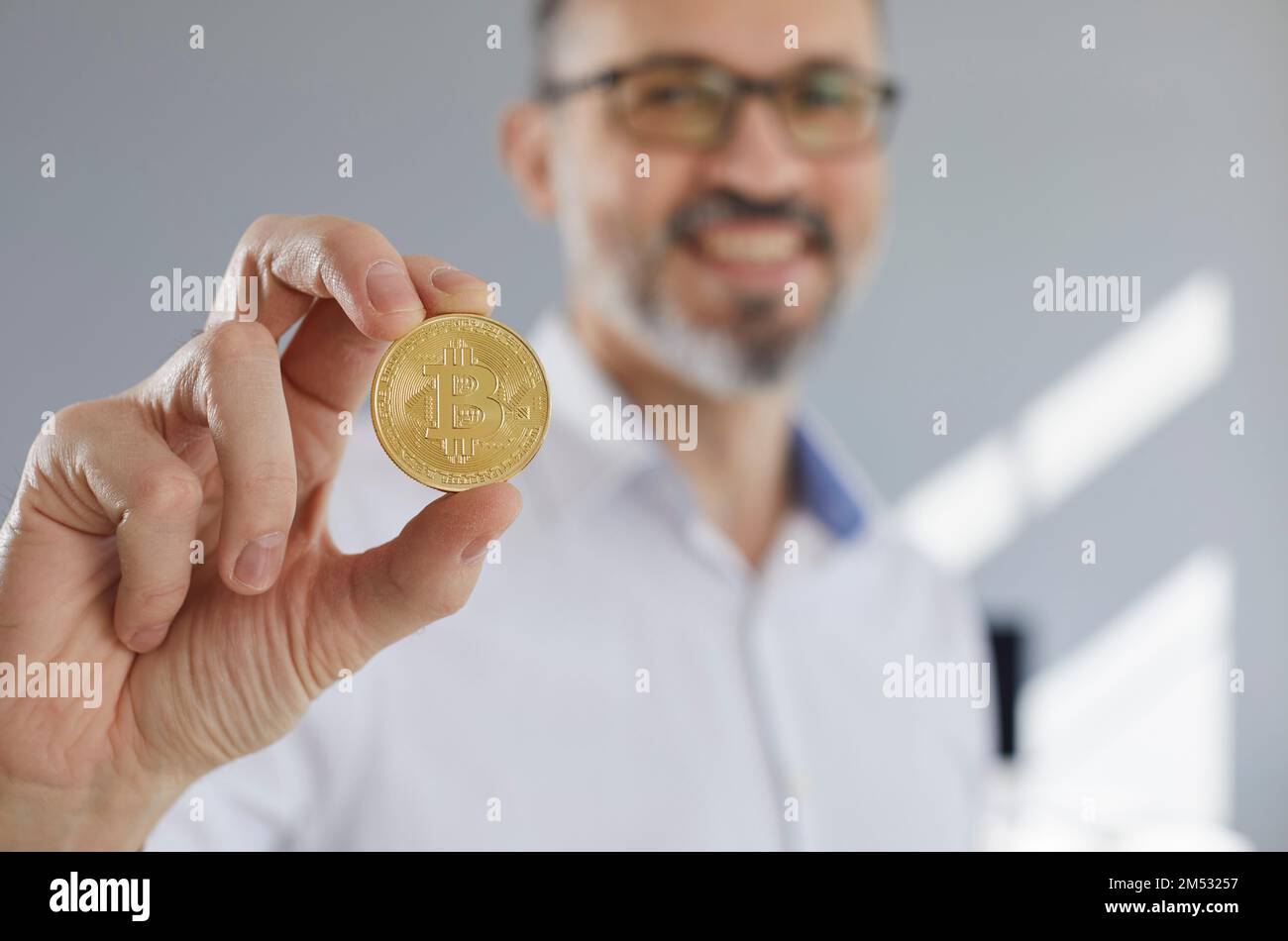 Nahaufnahme einer Münze mit einem Bitcoin-Symbol in der Hand eines glücklichen Geschäftsmannes Stockfoto