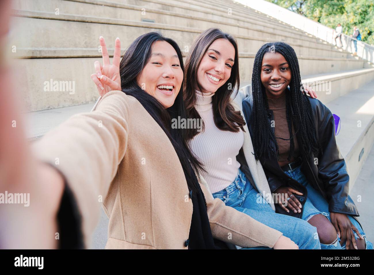 Fröhliche Gruppe multiethnischer junger Frauen, die ein Selfie-Porträt machen, das vor der Kamera lächelt. Drei verschiedene Mädchen, die draußen Spaß haben. Beste Freunde machen ein Foto. Hochwertiges Foto Stockfoto