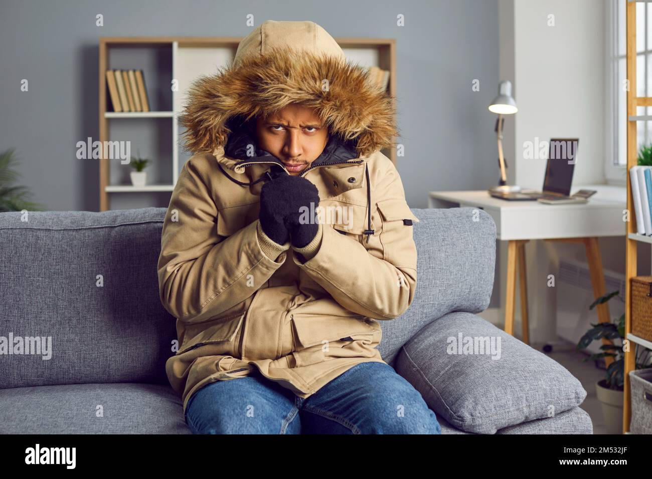 Junger Mann, der im kalten Winter erfriert und einen Mantel im Haus trägt, ohne Zentralheizung Stockfoto