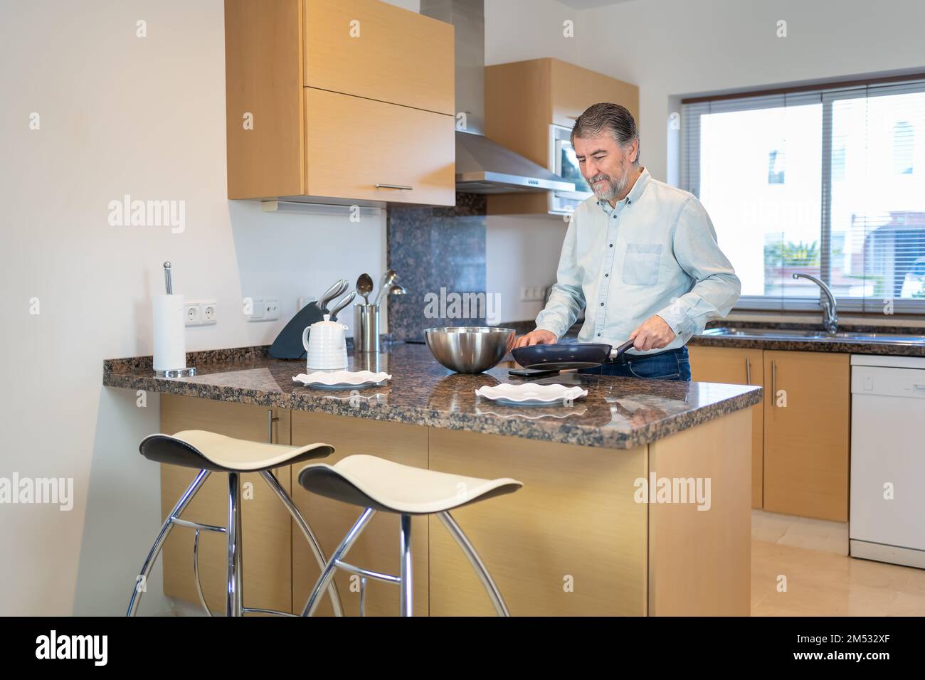 Ein älterer weißer Mann kocht mit einer Pfanne in der Hand in der Küche zu Hause. Stockfoto