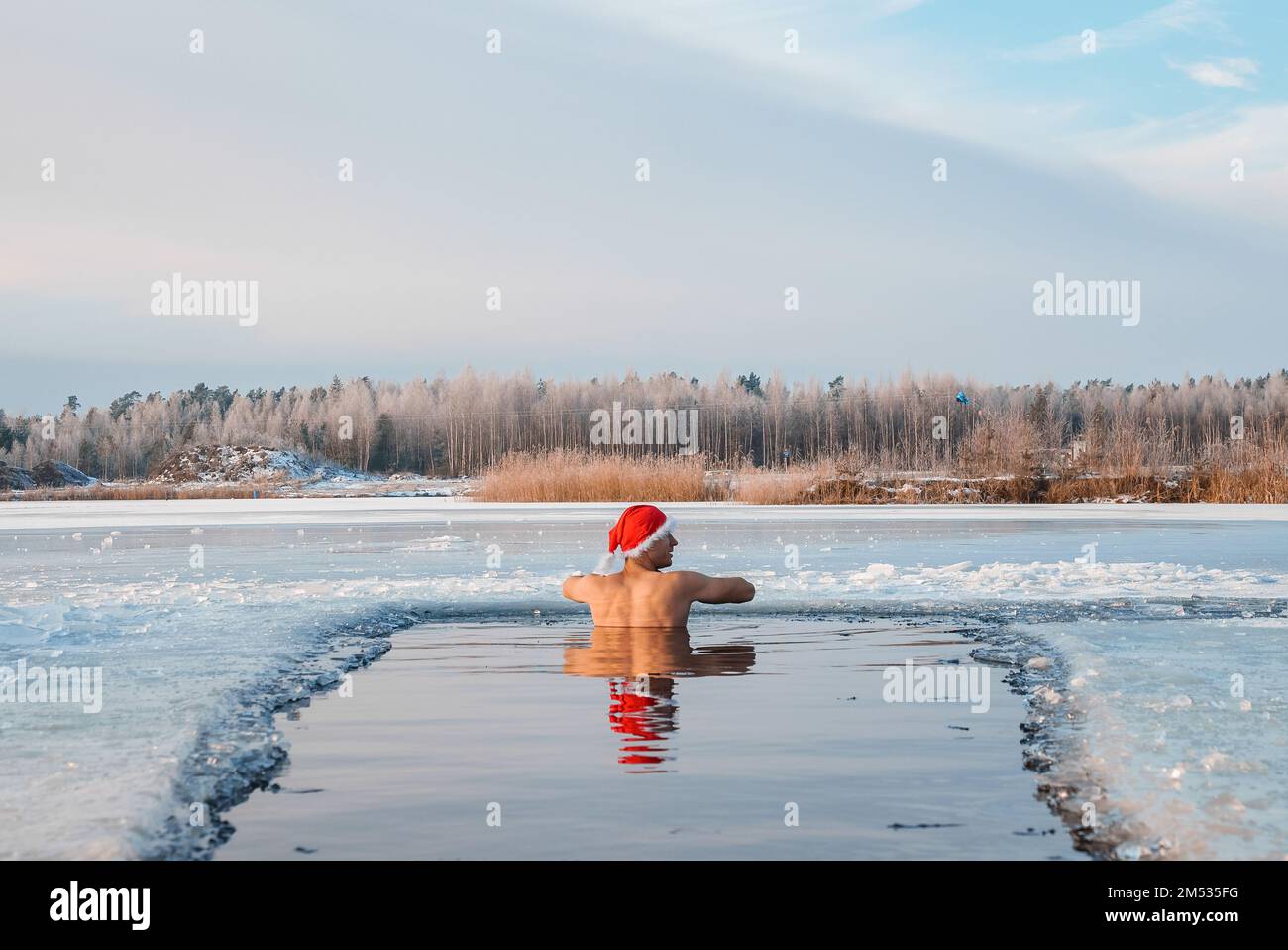 Ein junger Mann mit Weihnachtsmannmütze schwimmt in eiskaltem Wasser, umgeben von Eis. Stockfoto