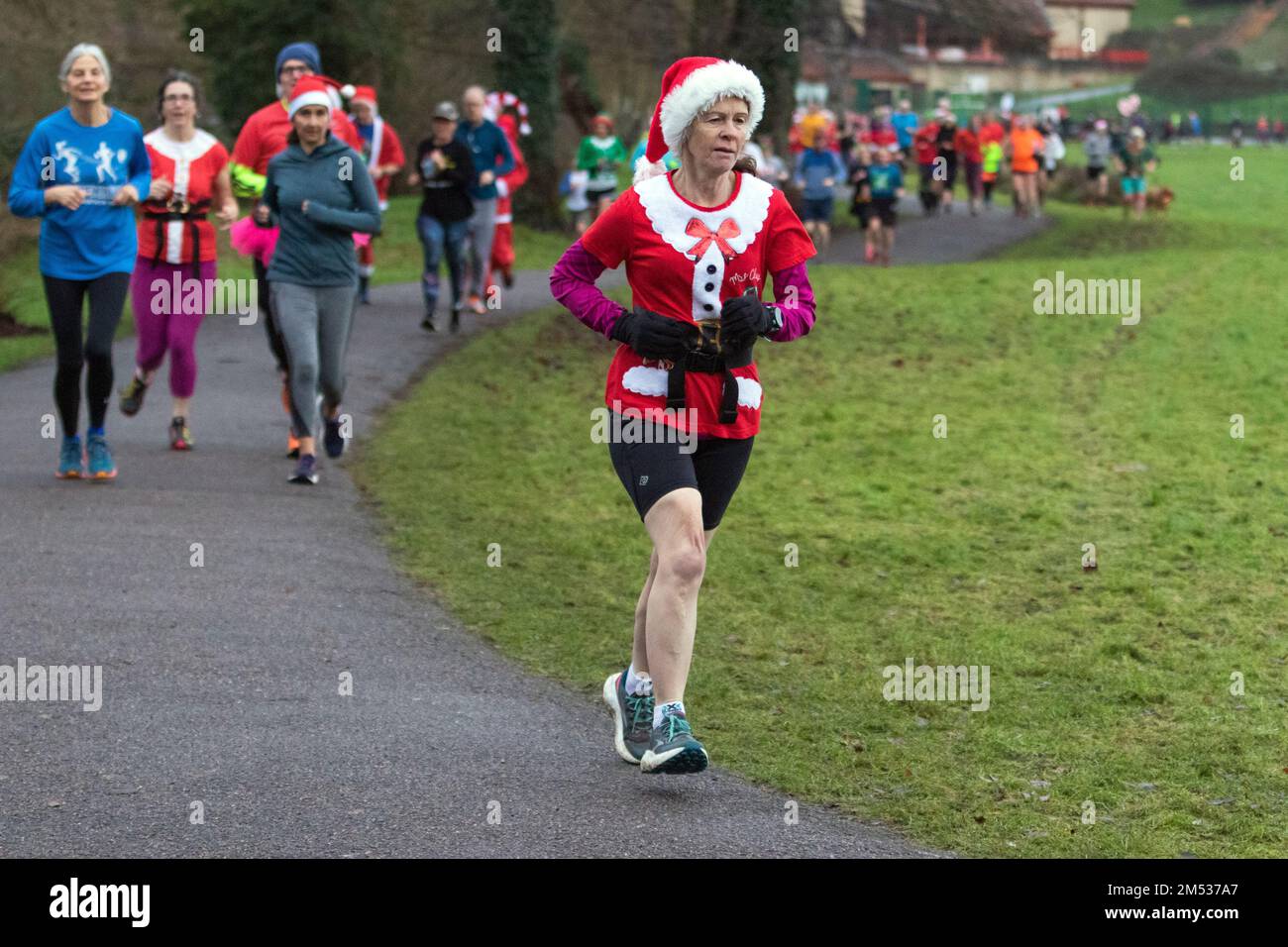 Chippenham, Wiltshire, Großbritannien. 25. Dezember 2022. Eine Läuferin in schicken Kleidern ist abgebildet, wenn sie an einer frühen Weihnachtstag 5km Parkrun in Monkton Park, Chippenham, Wiltshire, teilnimmt. Das feuchte Wetter hat die Stimmung der 200-300 Personen, die an der Veranstaltung teilgenommen haben, nicht geschwächt, viele von ihnen haben sich in schicken Kleidern verkleidet. Kredit: Lynchpics/Alamy Live News Stockfoto