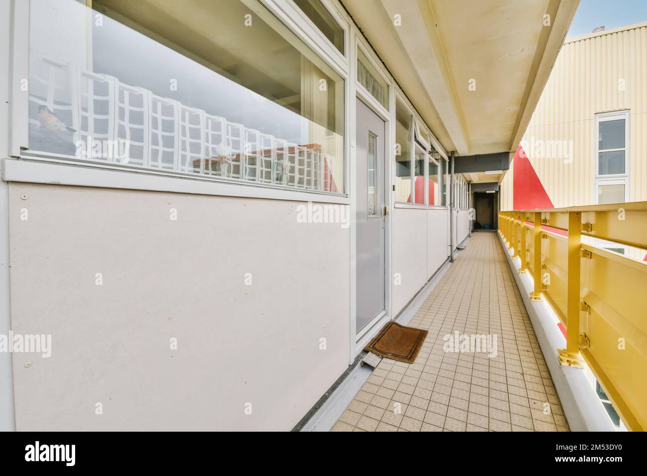 Ein Balkon mit gelben Geländern und weißen Zierleisten an der Seite eines Gebäudes, das so gestrichen wurde, als wäre es das Stockfoto