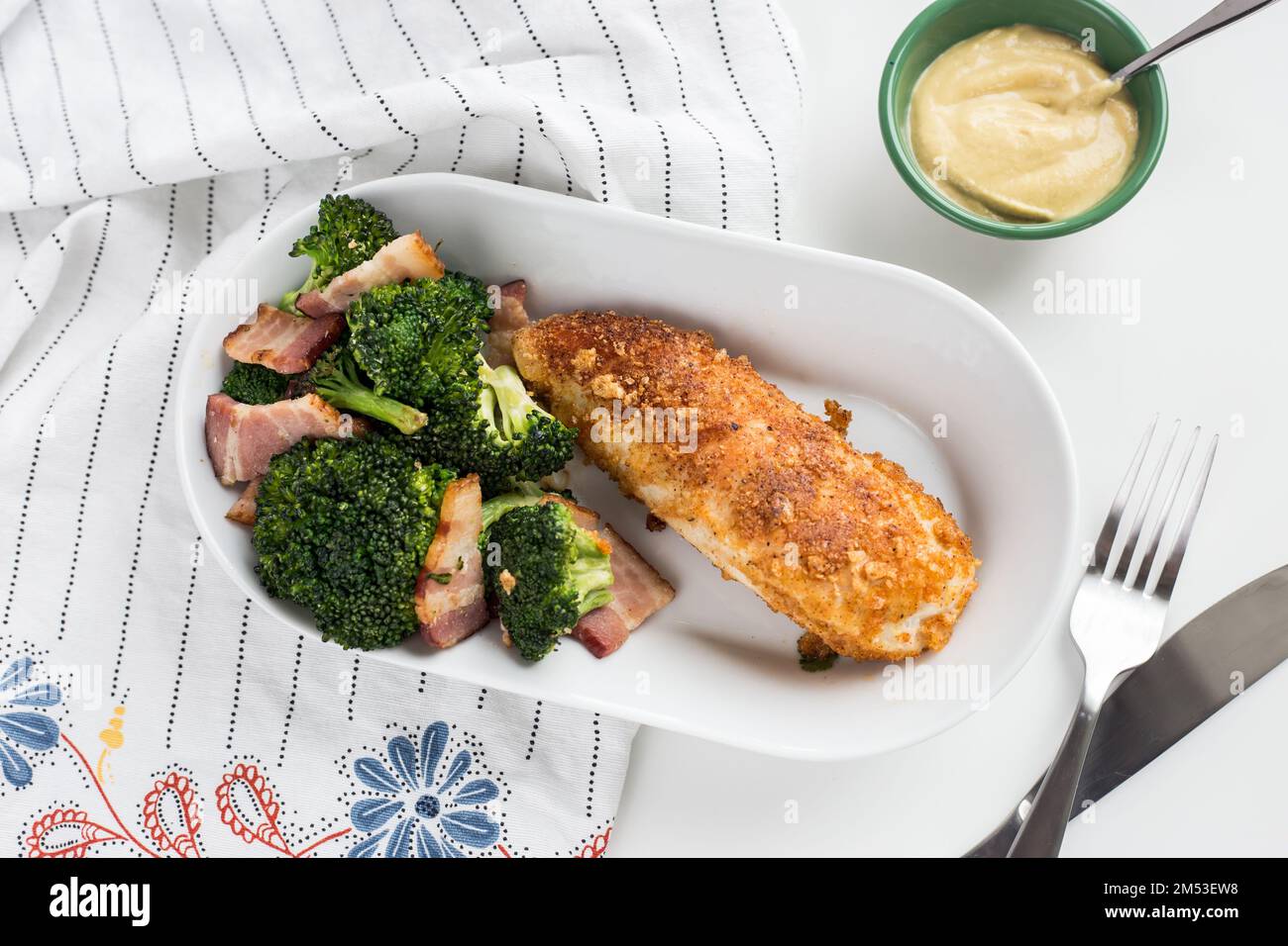 Ein Blick von oben auf das Huhn mit Brokkoli und Fleischscheiben auf einer weißen Schüssel mit einer Gabel und einem Messer neben einer gelben Sauce Stockfoto