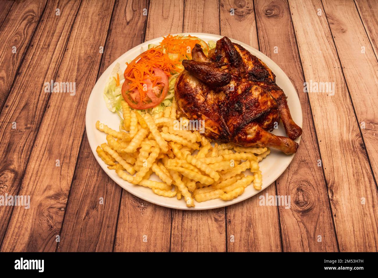 Ein gebratenes Hähnchen mit goldener Haut, dazu viele Pommes Frites und einen Salat und Tomatensalat Stockfoto