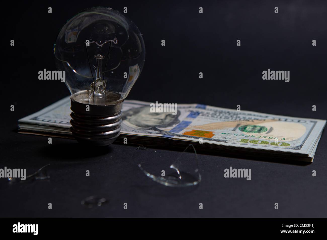 Kaputte Glühbirne mit Glasscherben auf 100-Dollar-Scheinen. Konzept der Strompreise und der Stromkrise in der Welt Stockfoto