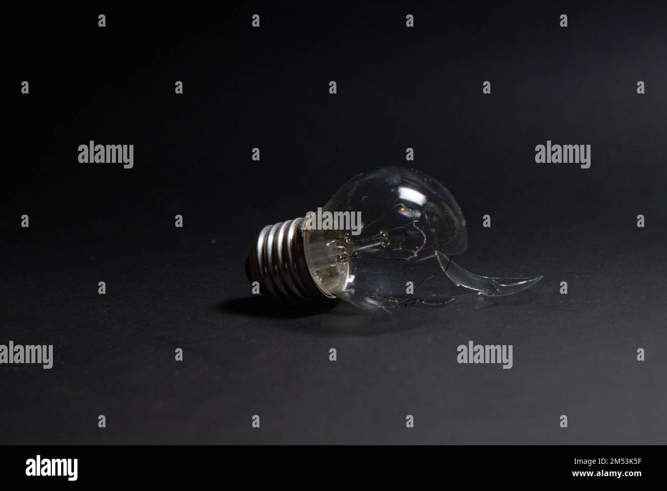 Gebrochene Glühlampe mit Glasscherben auf schwarzem Hintergrund. Das Konzept der Strompreise und die Stromversorgungskrise Stockfoto
